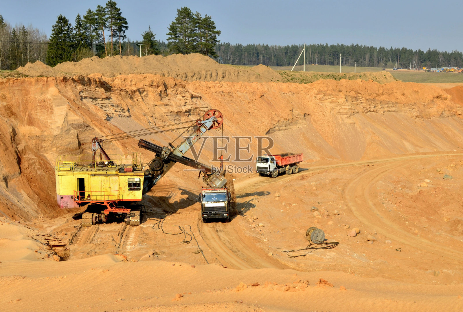 挖掘机在露天矿场向重型自卸卡车装载沙土照片摄影图片