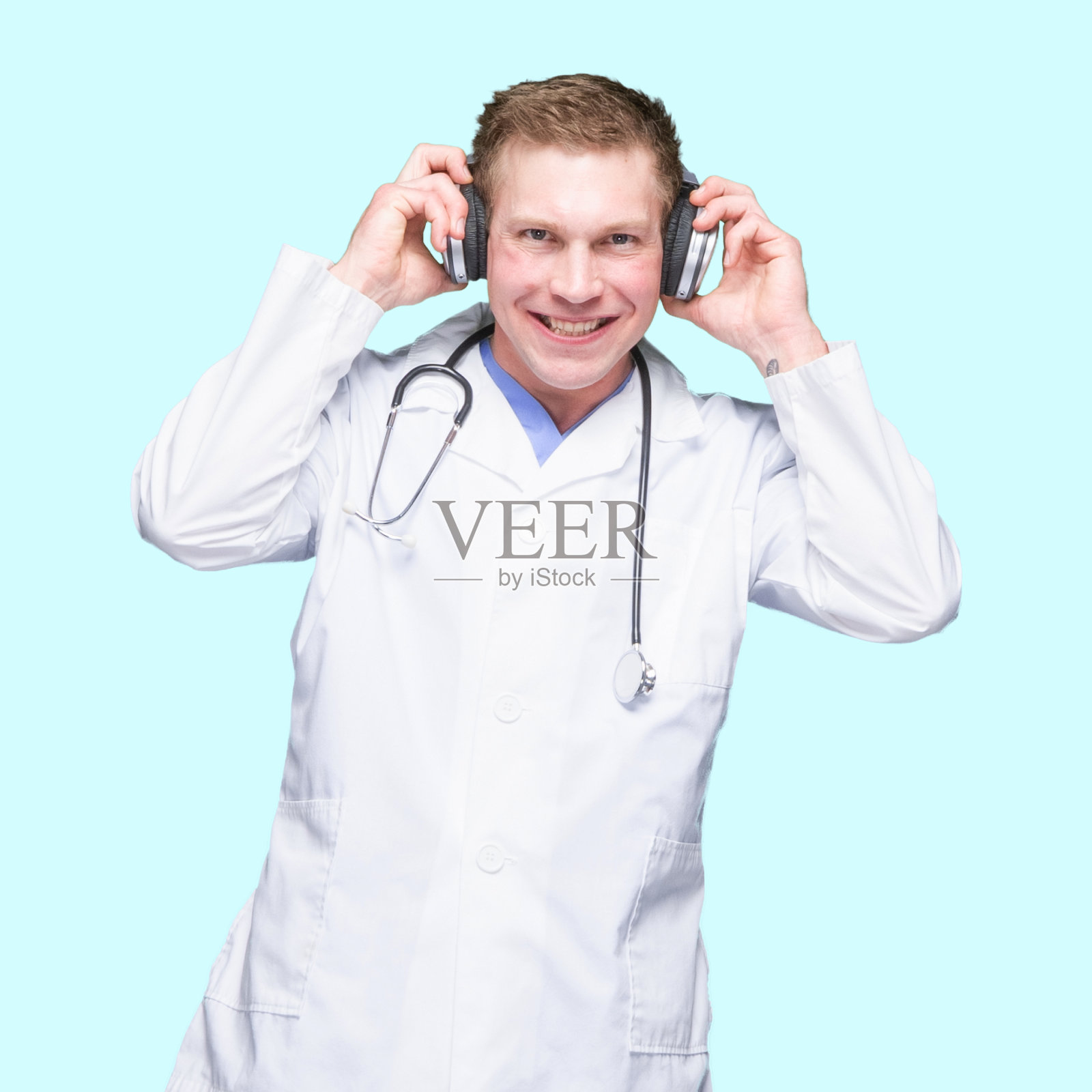 白人年轻男医生穿着实验服戴着耳机在有色背景前跳舞照片摄影图片