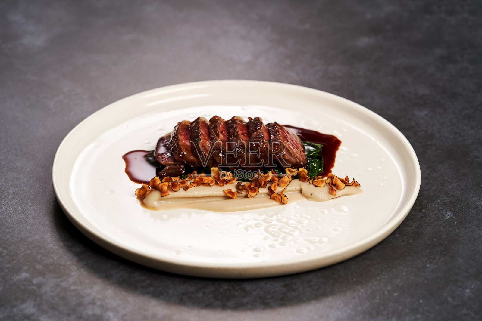 灰色的桌子上，白色的盘子里放着切片的羊肉和土豆泥照片摄影图片