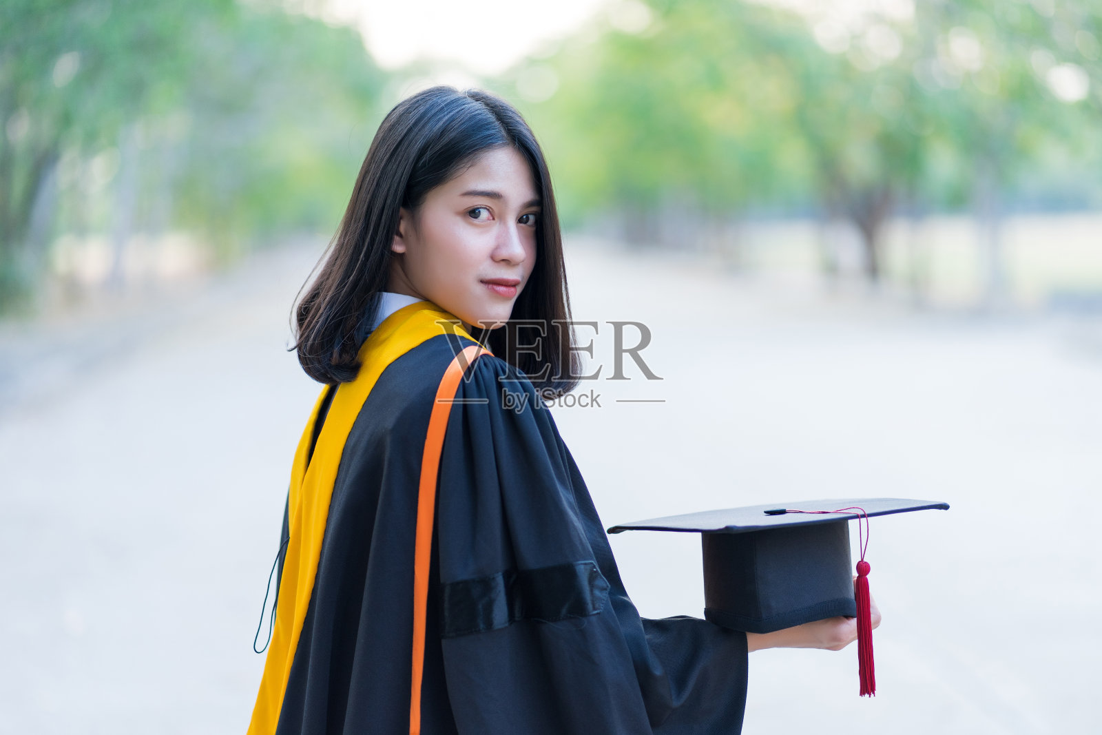 年轻快乐的女毕业生穿着学位服，拿着毕业帽，在大学校园的毕业典礼上庆祝获得大学学位的肖像照片摄影图片