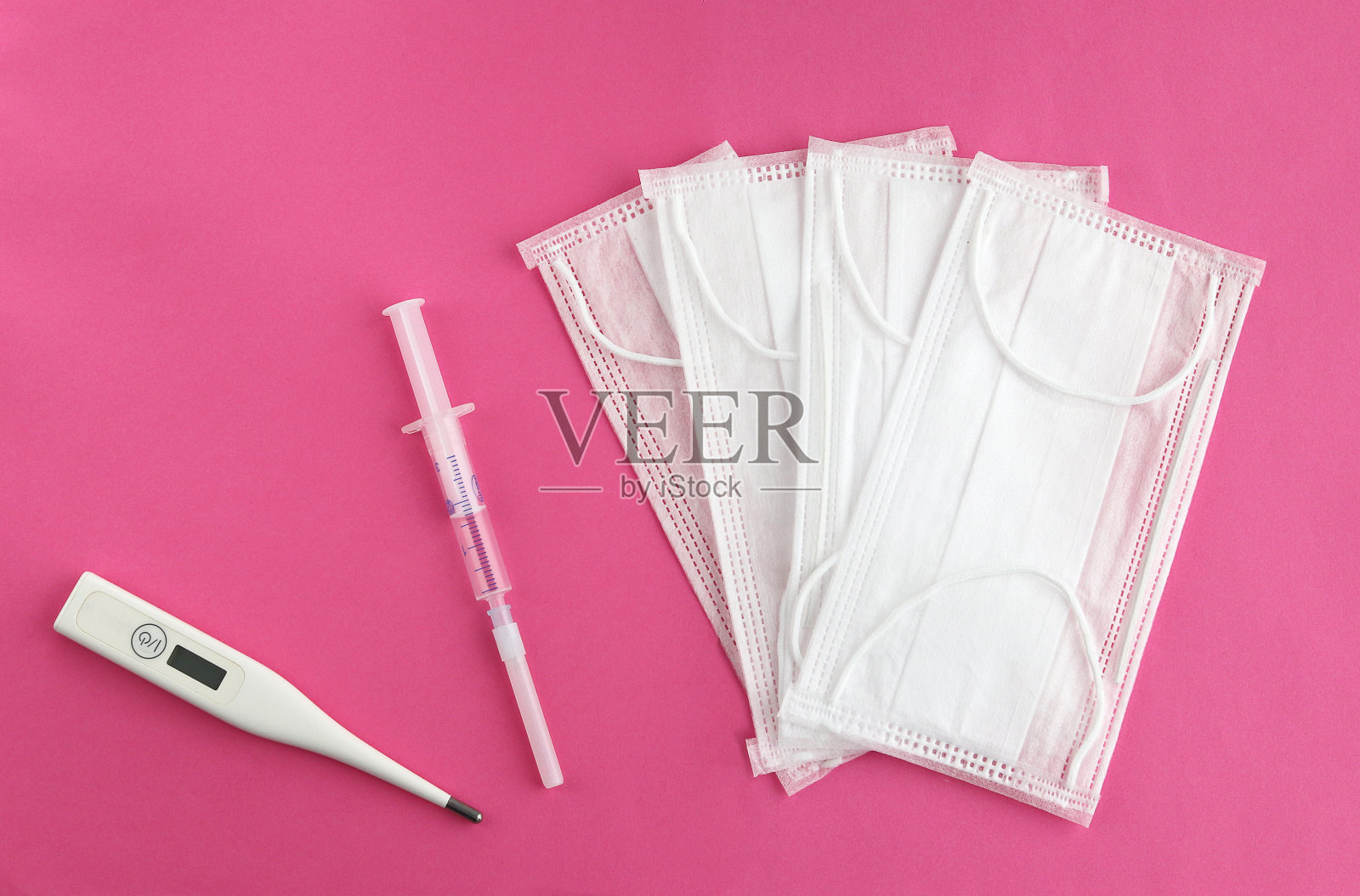 粉色背景上的医用口罩、温度计和注射器照片摄影图片