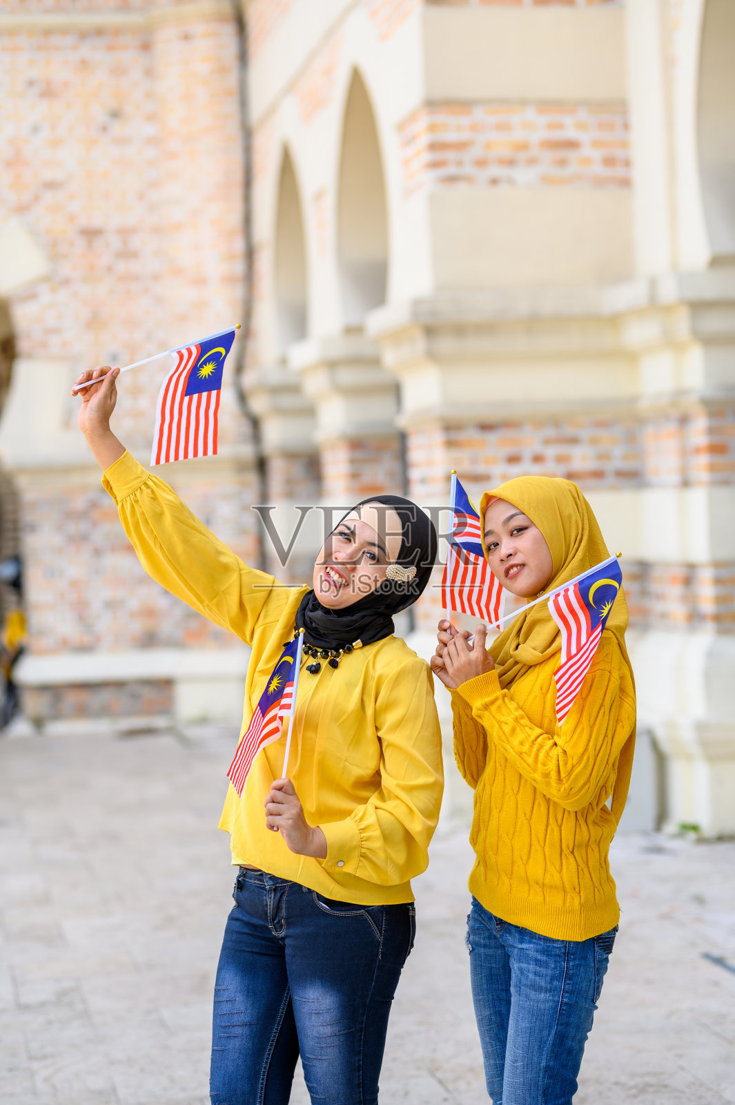 戴着头巾、手持马来西亚国旗的两名美丽的年轻穆斯林女性看着镜头照片摄影图片