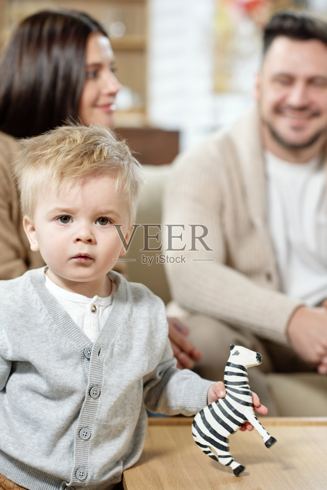 可爱的男婴抱着斑马玩具，父母在背景中看着镜头照片摄影图片