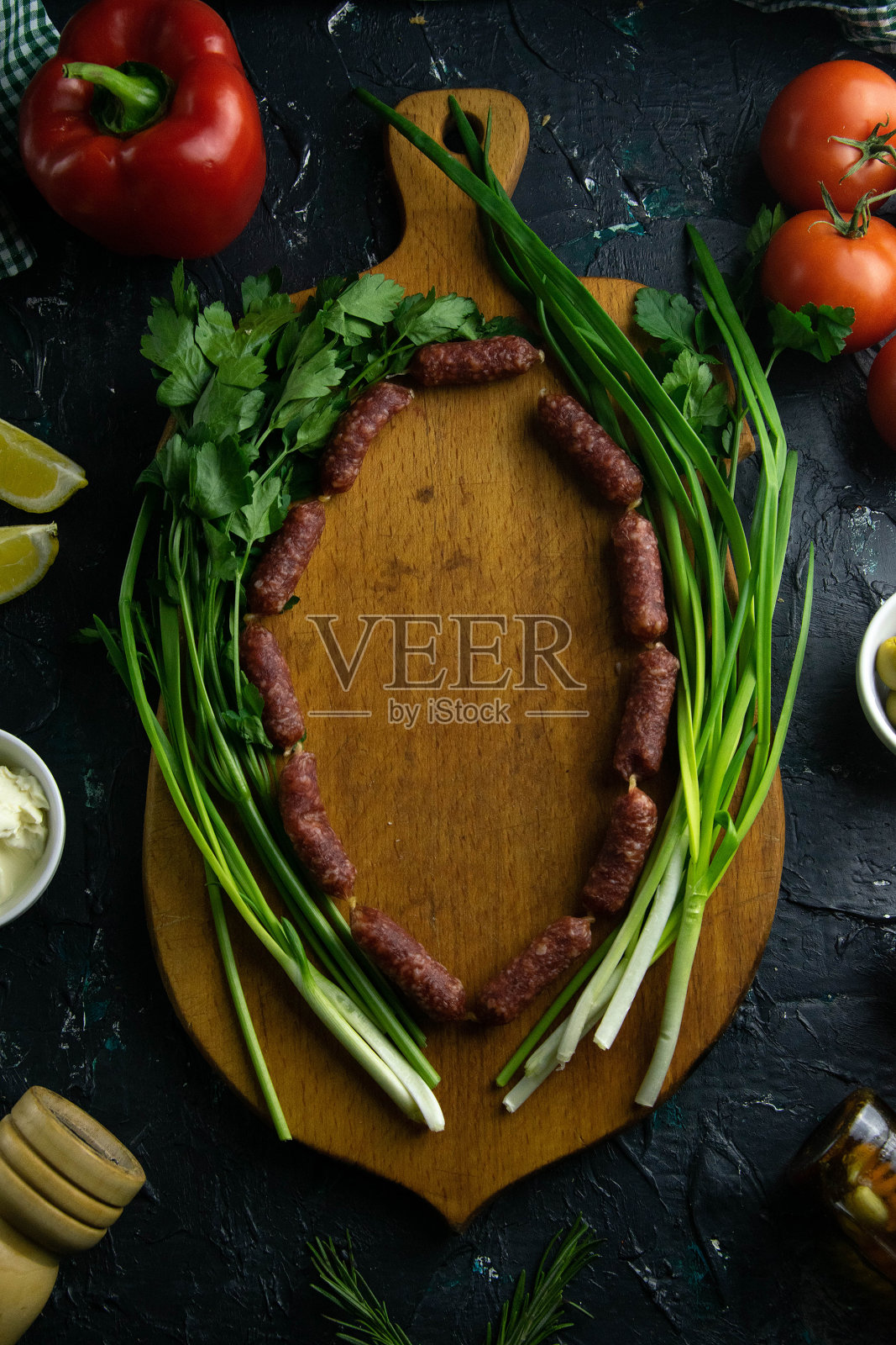 在一块木板上清理出空间，环绕香肠、绿洋葱、番茄、酱料、橄榄、柠檬、香料和莳萝照片摄影图片