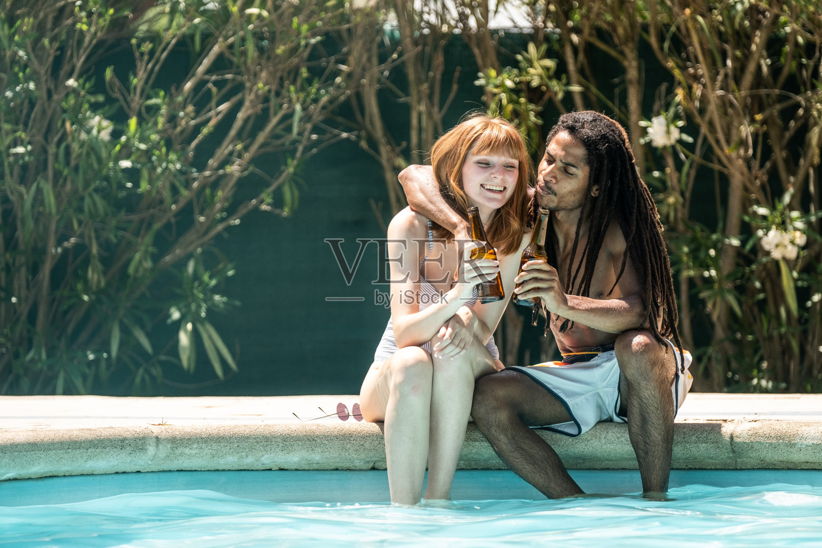 非裔美国男人和白人女人在泳池边用啤酒瓶碰杯照片摄影图片
