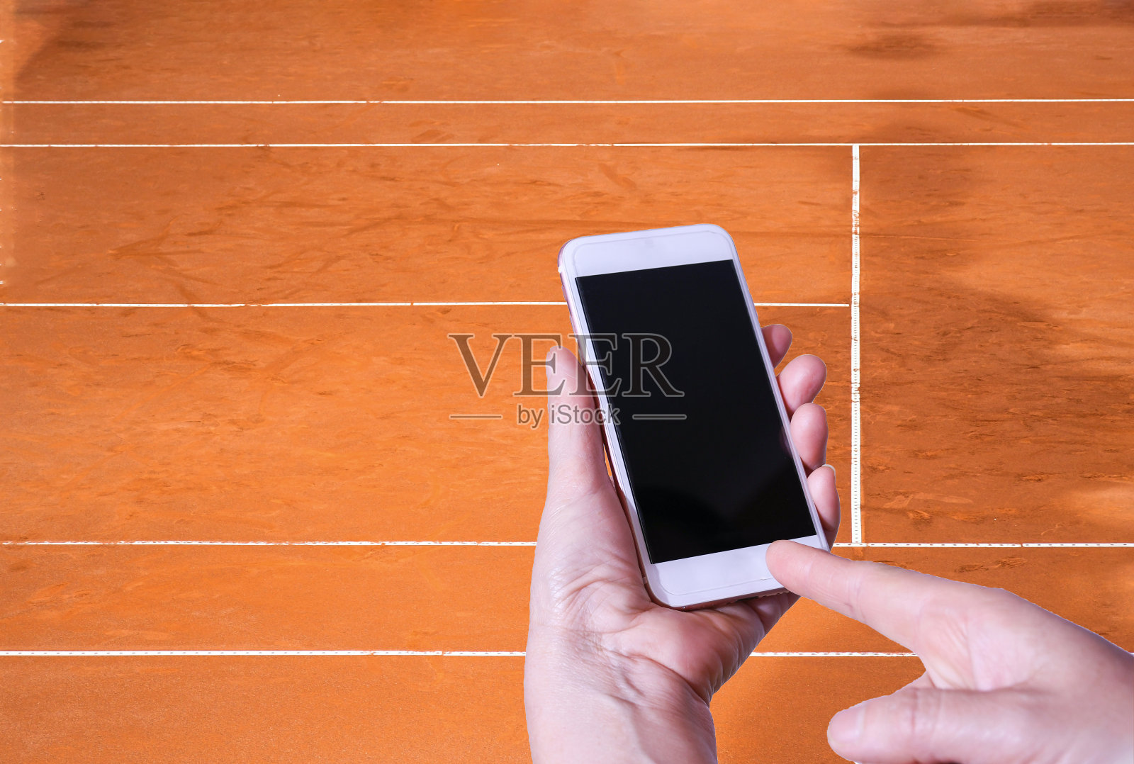 手用智能手机与背景空网球场，棕色地板和白线。运动和技术背景概念。照片摄影图片