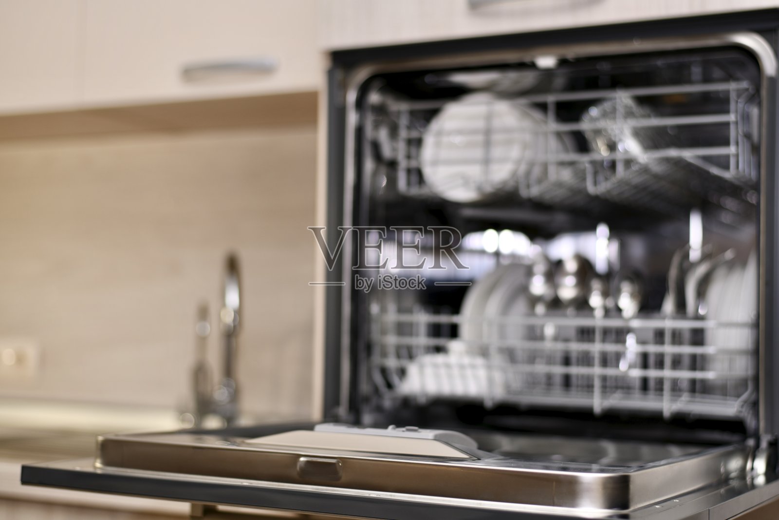 一个洗碗机，在水槽的高度有一个开放式的盘子，一个烘干机和两个水龙头，作为一个模糊的背景与散景。照片摄影图片