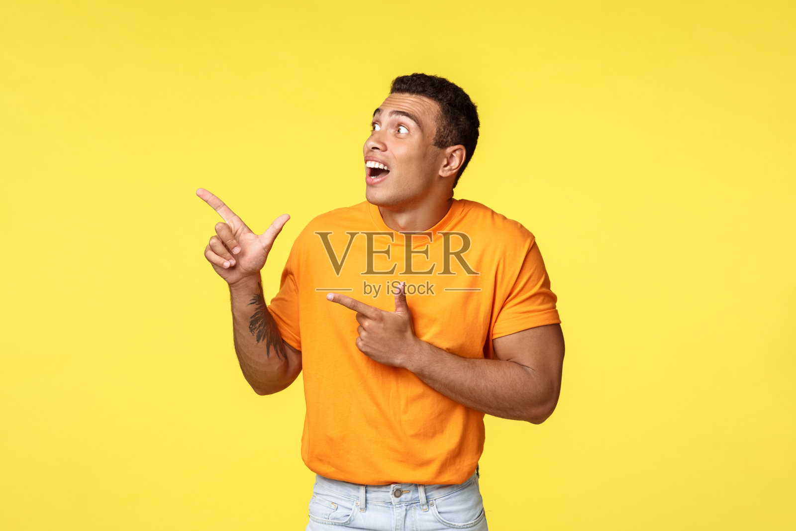 惊讶，兴奋的英俊男子穿着橙色T恤，喘着气，着迷，盯着左上角的一个梦幻般的促销活动，看到新年倒计时期间惊艳的烟花照片摄影图片