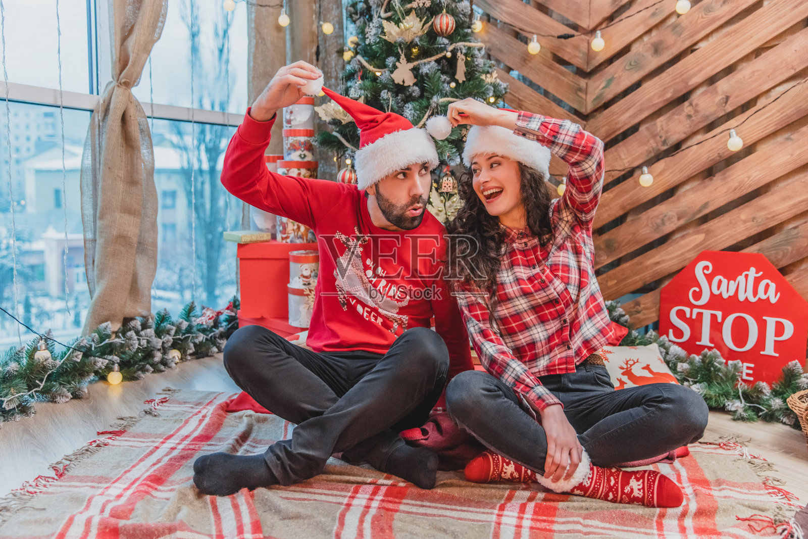 酷酷有趣好玩的伙伴穿着红色针织服装和圣诞老人帽正在做滑稽的鬼脸，胡闹。照片摄影图片