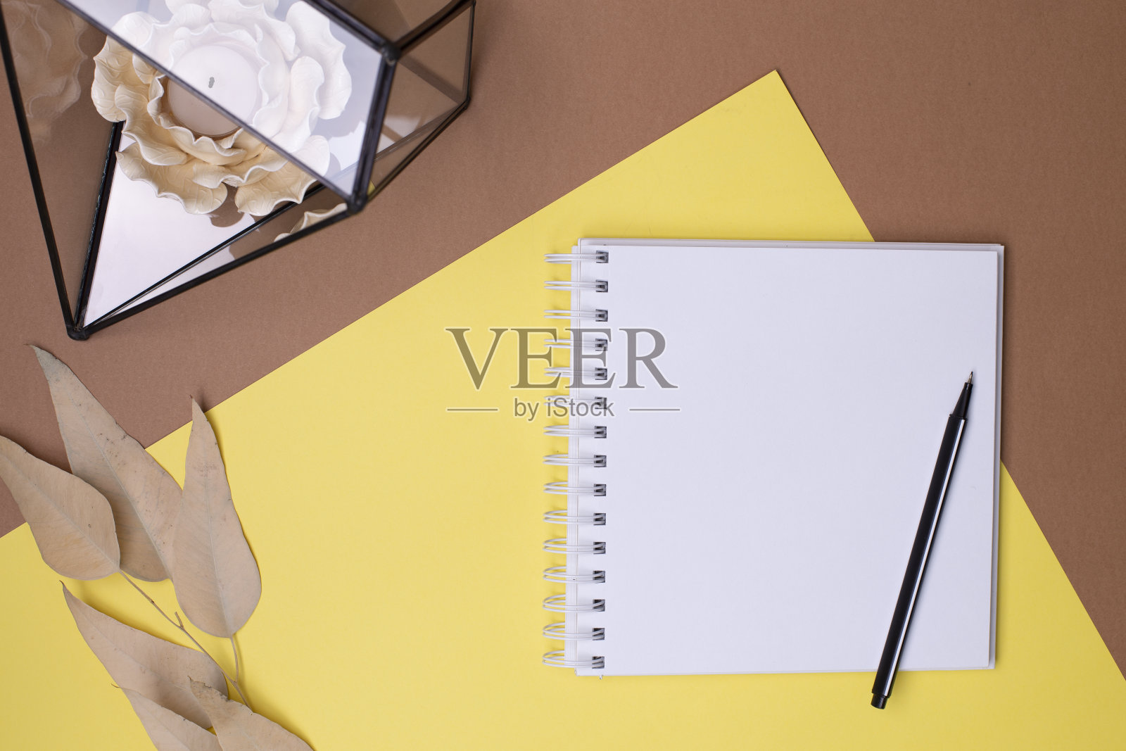 俯视图的一个空日记本和钢笔，米色的叶子，玻璃花卉与蜡烛的形状的花在一个组合的黄色和棕色的背景，文字的地方照片摄影图片