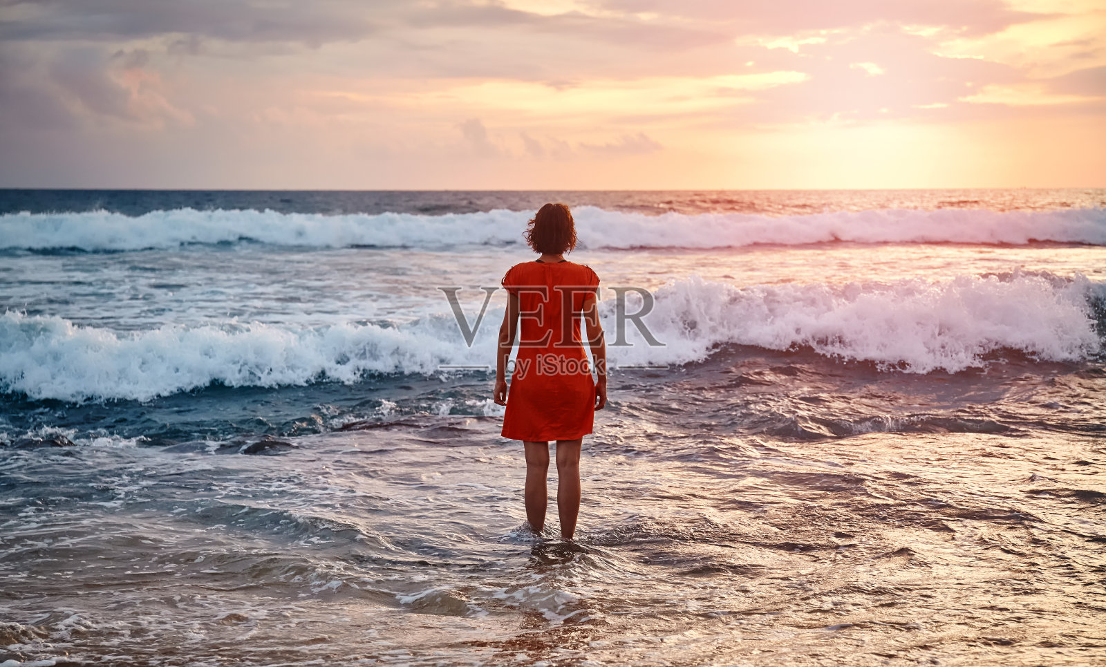 日落时分，穿着橙色连衣裙静静地站在海边的女人照片摄影图片