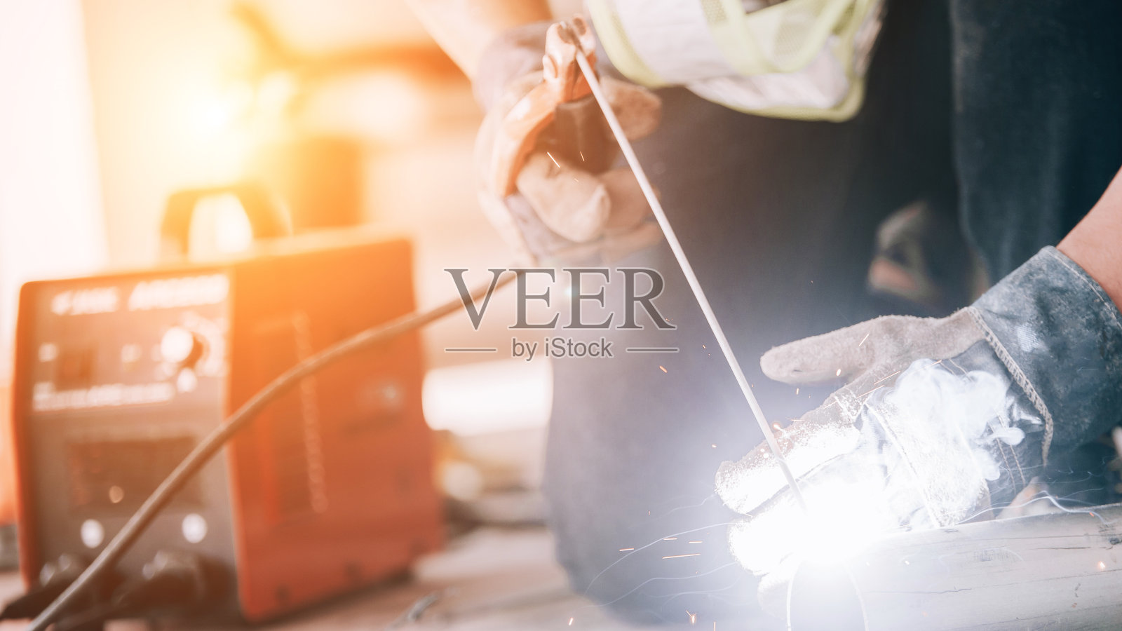 身穿防护服和面罩的焊接工人在工业台上焊接金属管，火花飞溅。照片摄影图片