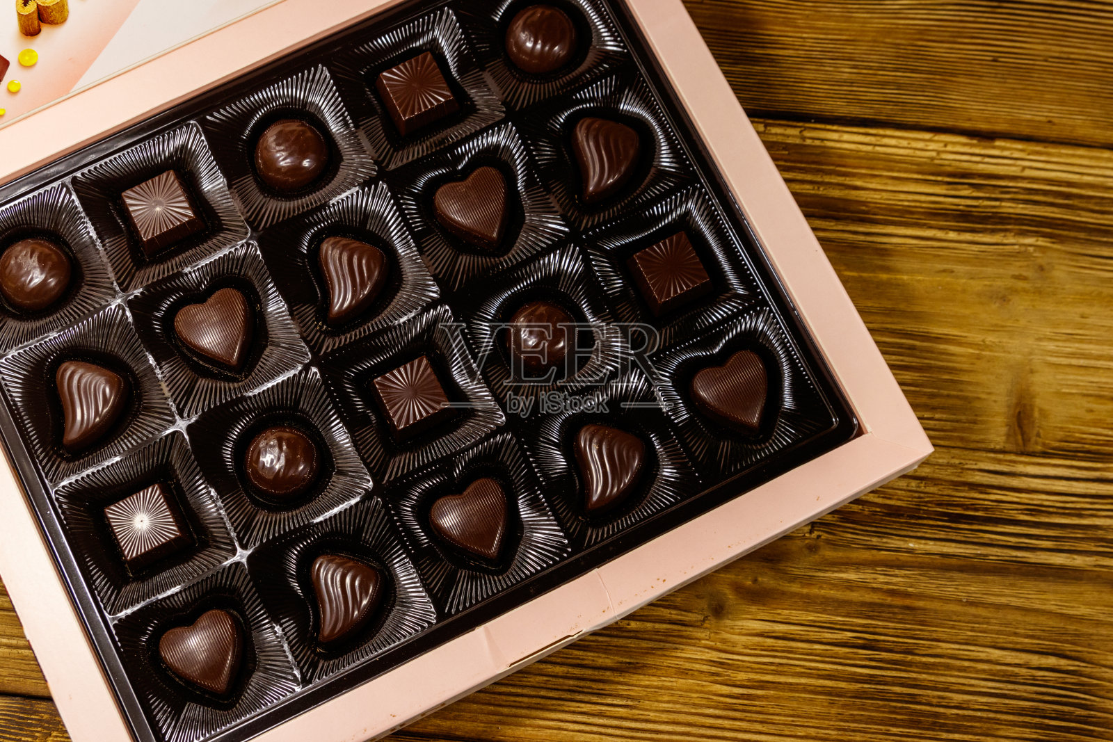 木桌上的盒子里装着各式各样的巧克力糖果。俯视图照片摄影图片