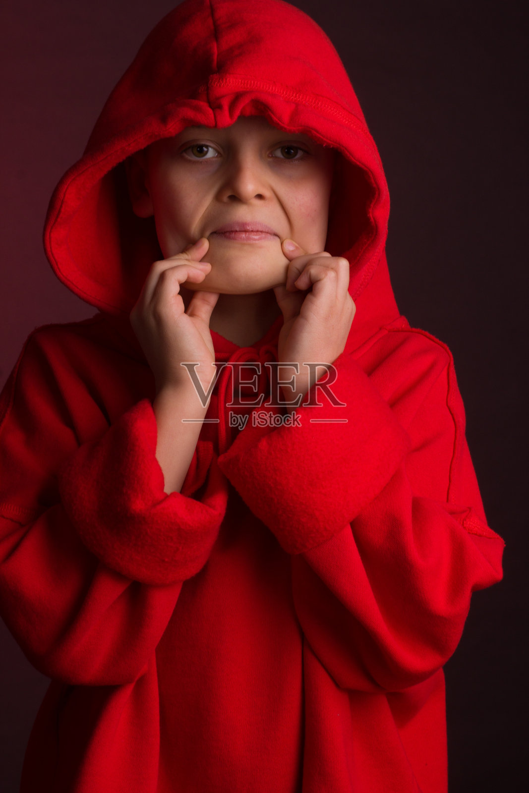 在栗色背景下，身穿红色连帽衫的黑发男孩的影棚画像照片摄影图片