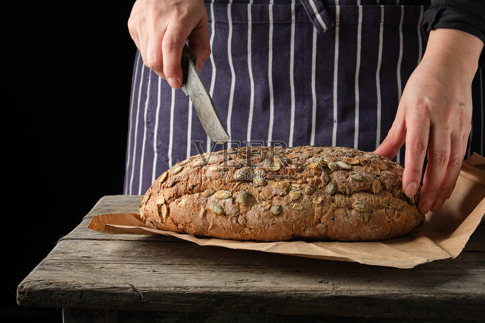 穿着蓝色围裙，手持刀准备切圆面包的女人照片摄影图片