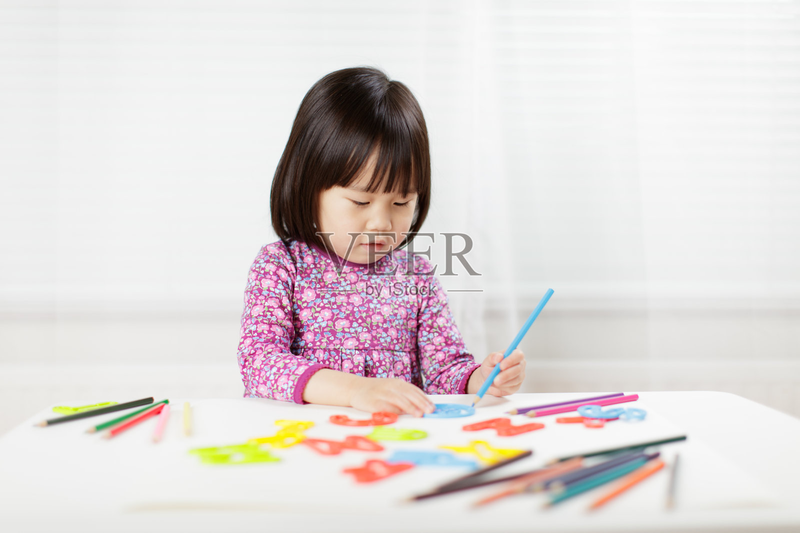 蹒跚学步的小女孩练习在白色背景的白纸上写字照片摄影图片