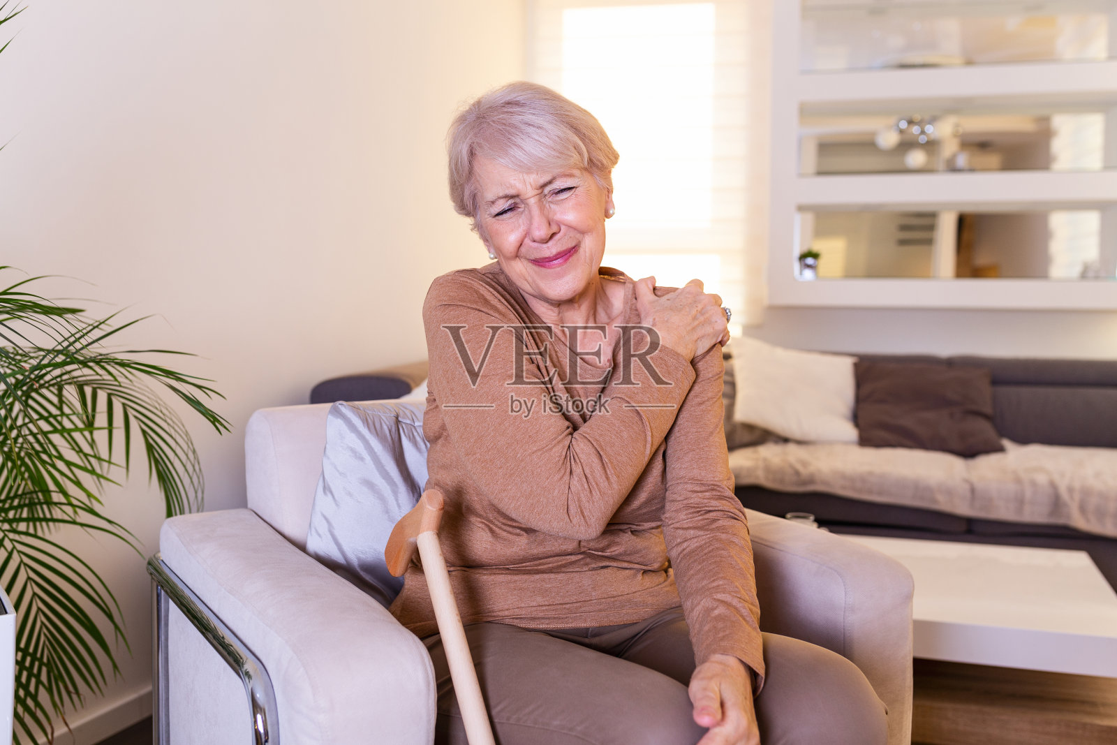 在家忍受肩膀疼痛的老年妇女。资深女士正在展示她的肩膀疼痛照片摄影图片