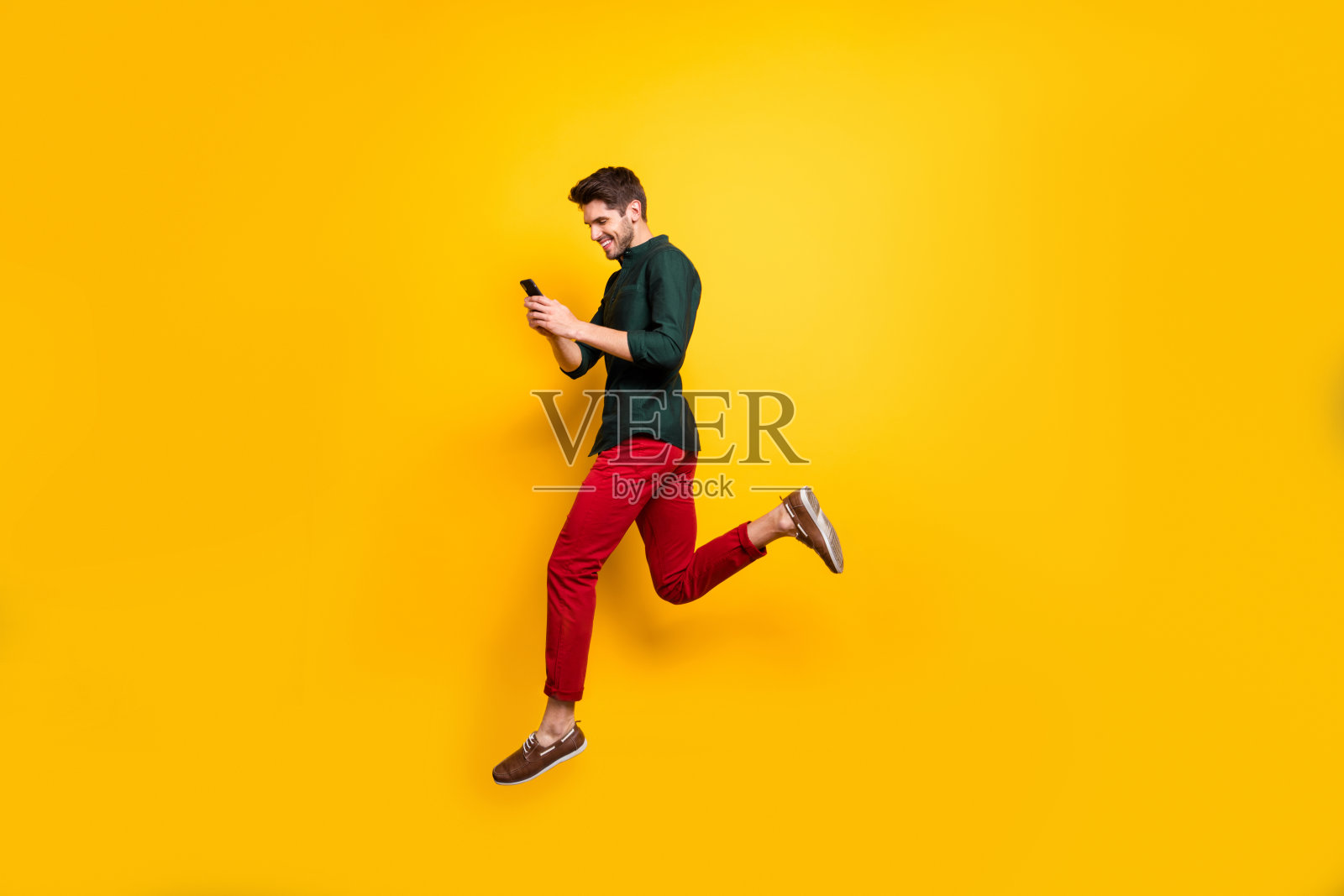 简介侧全身尺寸照片开朗积极的男人跑步跳跃沉迷于他的手机渴望销售孤立明亮的颜色背景照片摄影图片