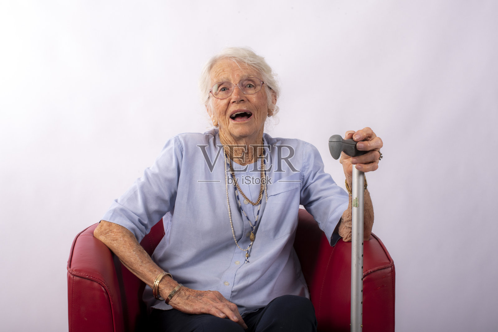 拄着拐杖的老妇人坐在红色的椅子上。照片摄影图片