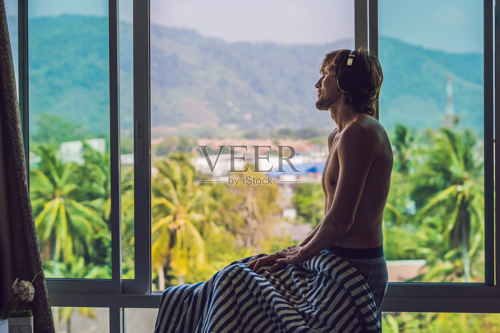 在山景窗户背景下，戴着无线耳机听音乐的男人照片摄影图片