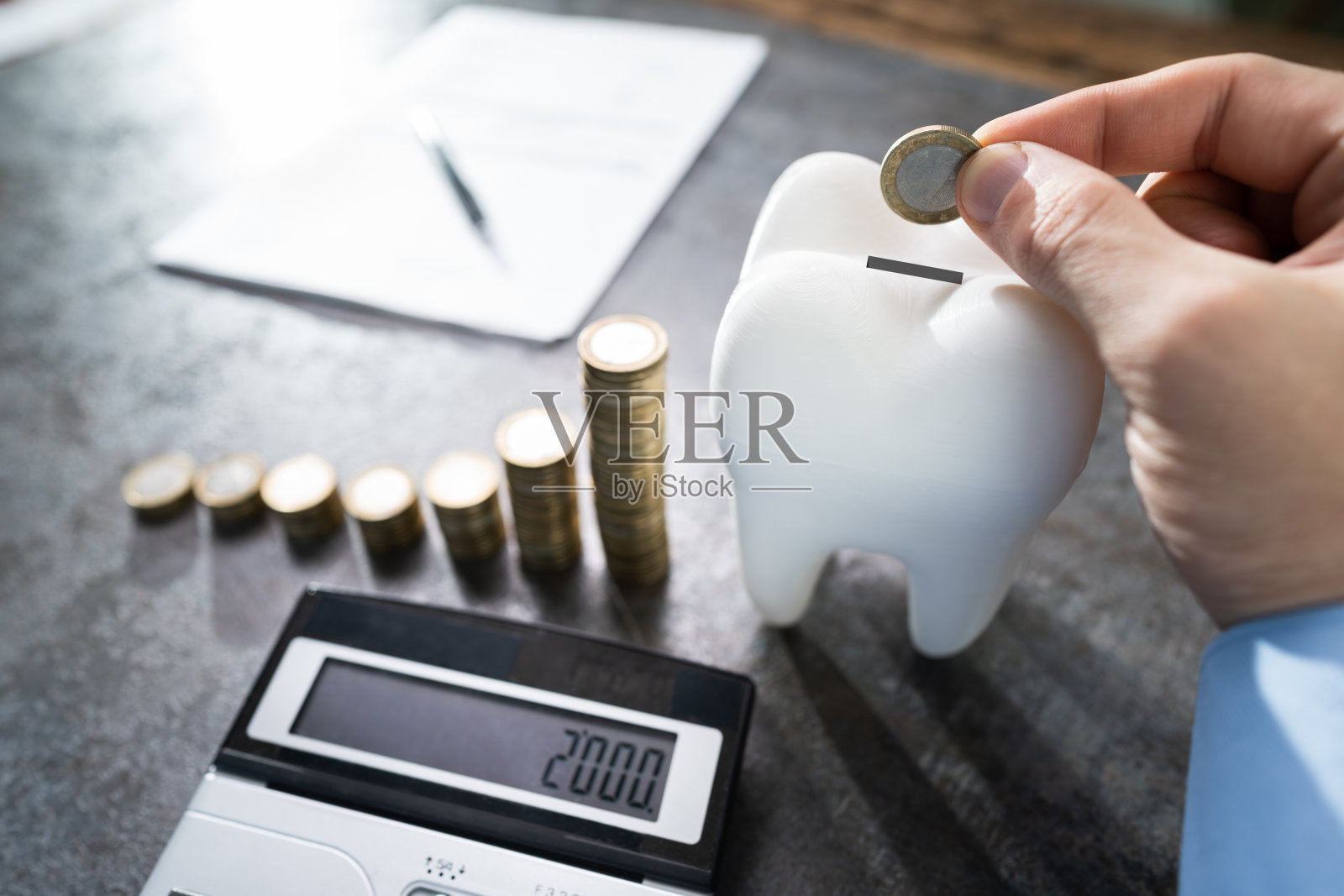 男人将硬币投入牙齿形状的储蓄罐照片摄影图片