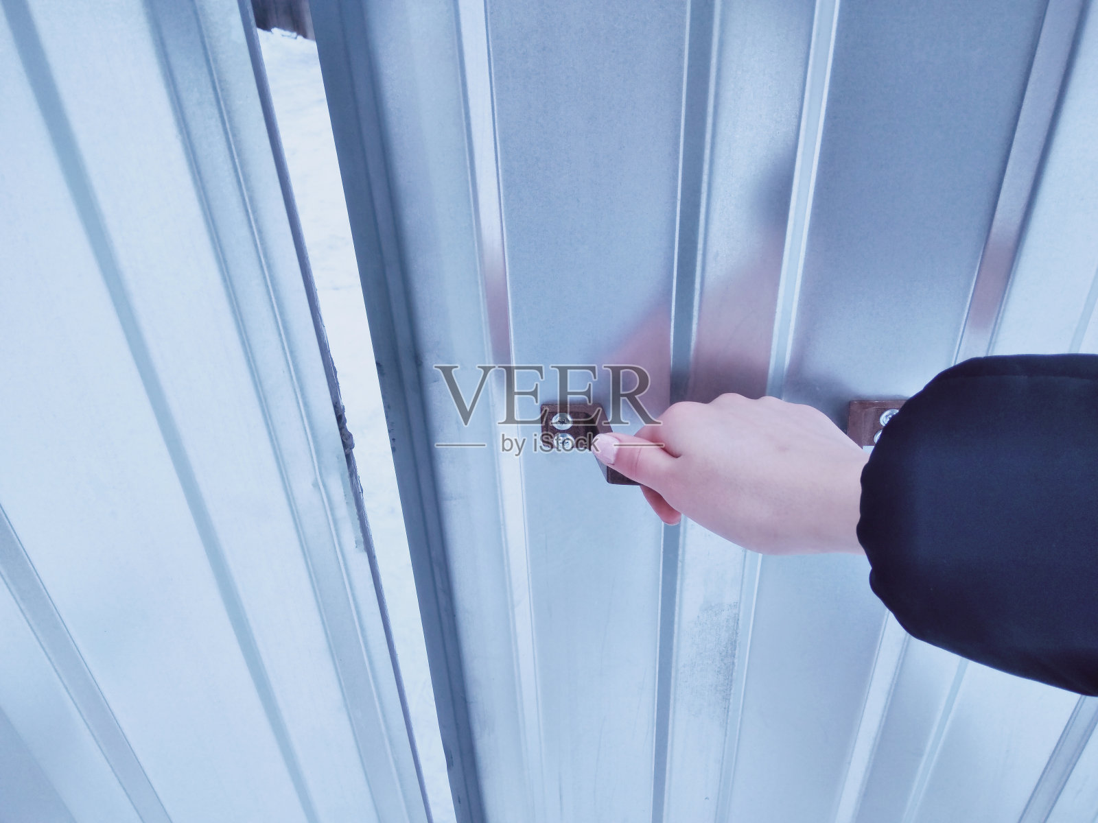 女人打开铁栅栏的金属门。冬天，女人握住把手关门。照片摄影图片