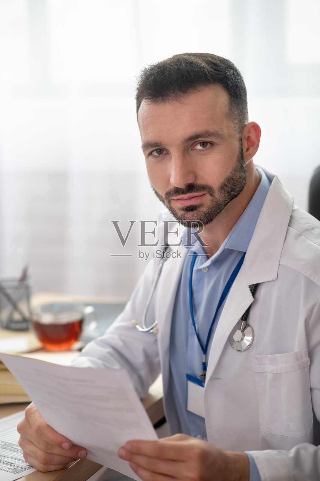 身穿白大褂的年轻络腮胡医生正在喝早茶照片摄影图片