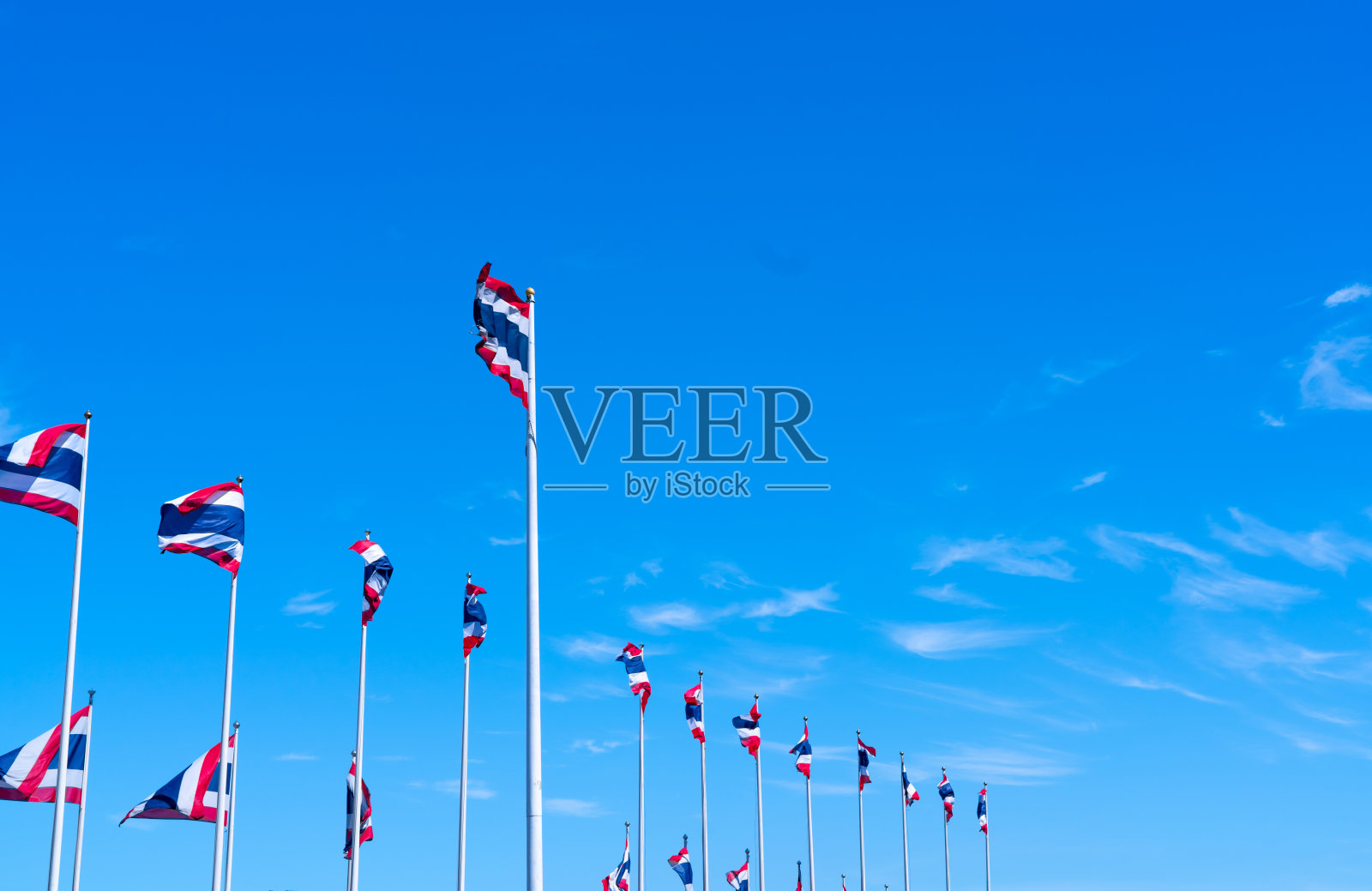 许多泰国国旗在蓝色的天空中飘扬。一面泰国国旗被拉到旗杆顶端。红、蓝、白三色长方形织物。泰国王国国旗。照片摄影图片