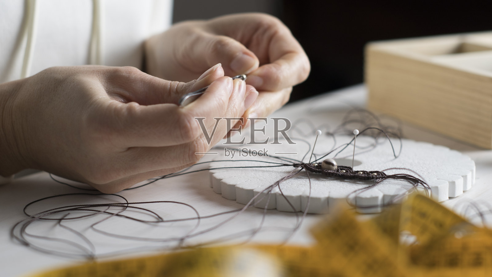 生活方式概念：在家工作重塑生活，女人用双手在浅色木桌上用石头珠子和工具制作马卡龙结饰品照片摄影图片