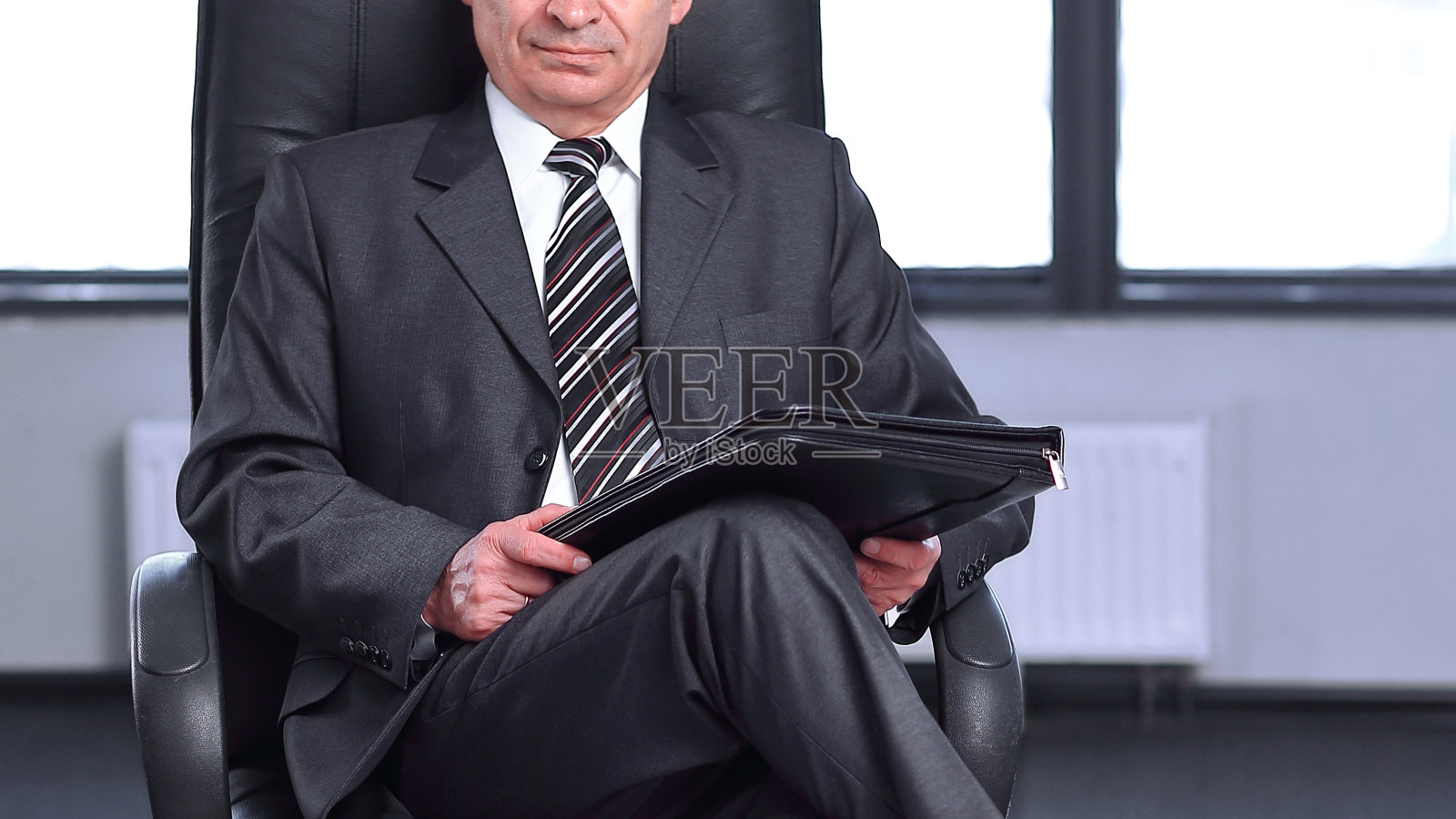 拿着皮革文件夹坐在办公室里的自信商人照片摄影图片
