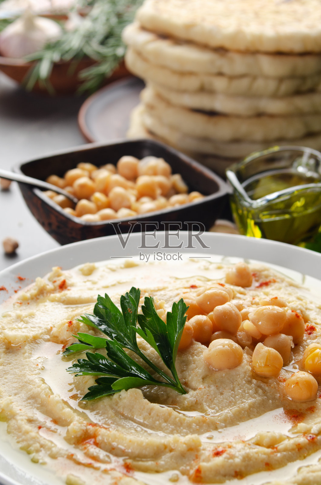 低角度的鹰嘴豆泥，橄榄油和绿香菜叶放在石头桌上，皮塔饼放在一边照片摄影图片