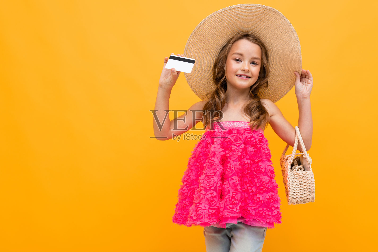 白人女孩戴着草帽，带着一个圆袋子，拿着一张黄色背景上的信用卡照片摄影图片