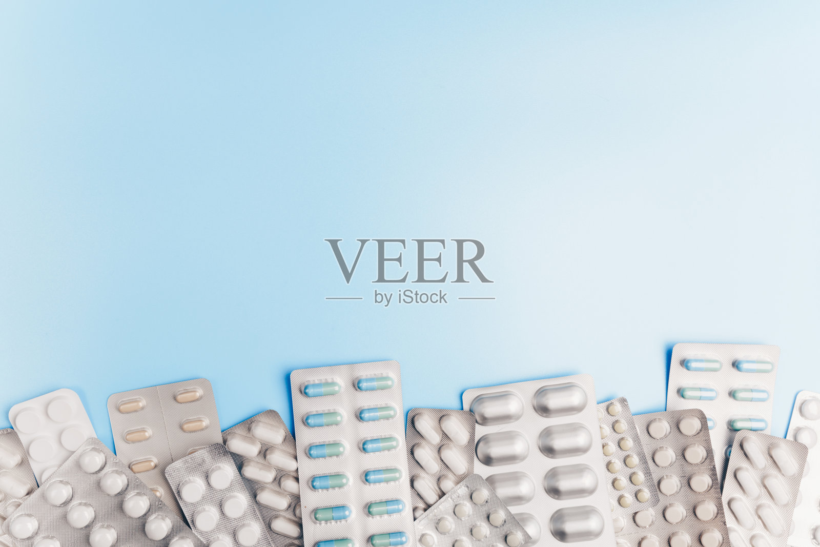 浅蓝色背景上有许多不同包装的药片。照片摄影图片