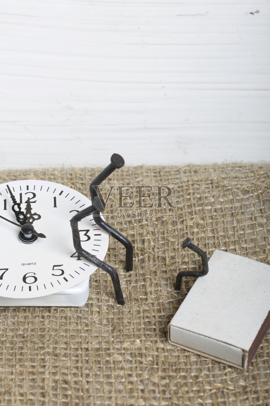 用木钉做成的人造小雕像。他们坐在表盘上，彼此挨着。对面，一个孩子的身影正坐在钉子上。爱的象征和无情的时间流逝。照片摄影图片