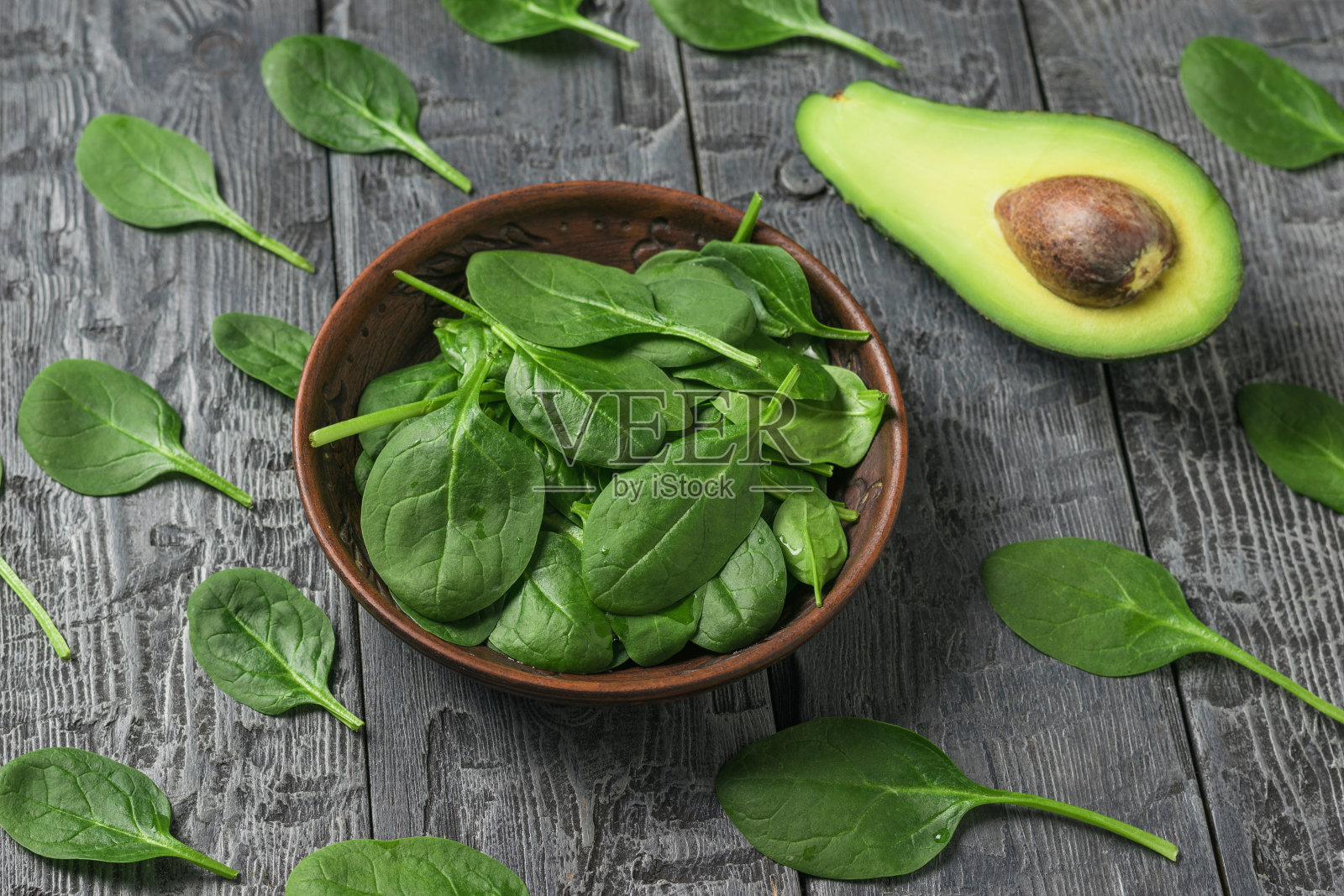 木桌上放着一碗菠菜叶和半个鳄梨。照片摄影图片