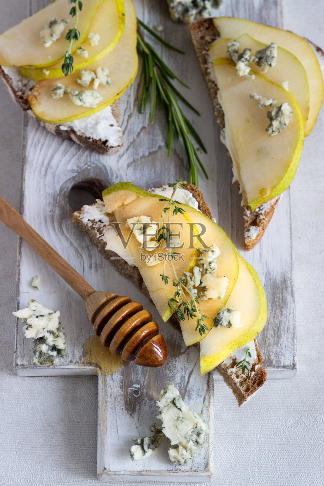 烤面包或意式烤面包配乳清干酪或奶油奶酪，梨，蜂蜜和蓝奶酪放在白色的木板上。美味的早餐或零食在一个明亮的背景。照片摄影图片