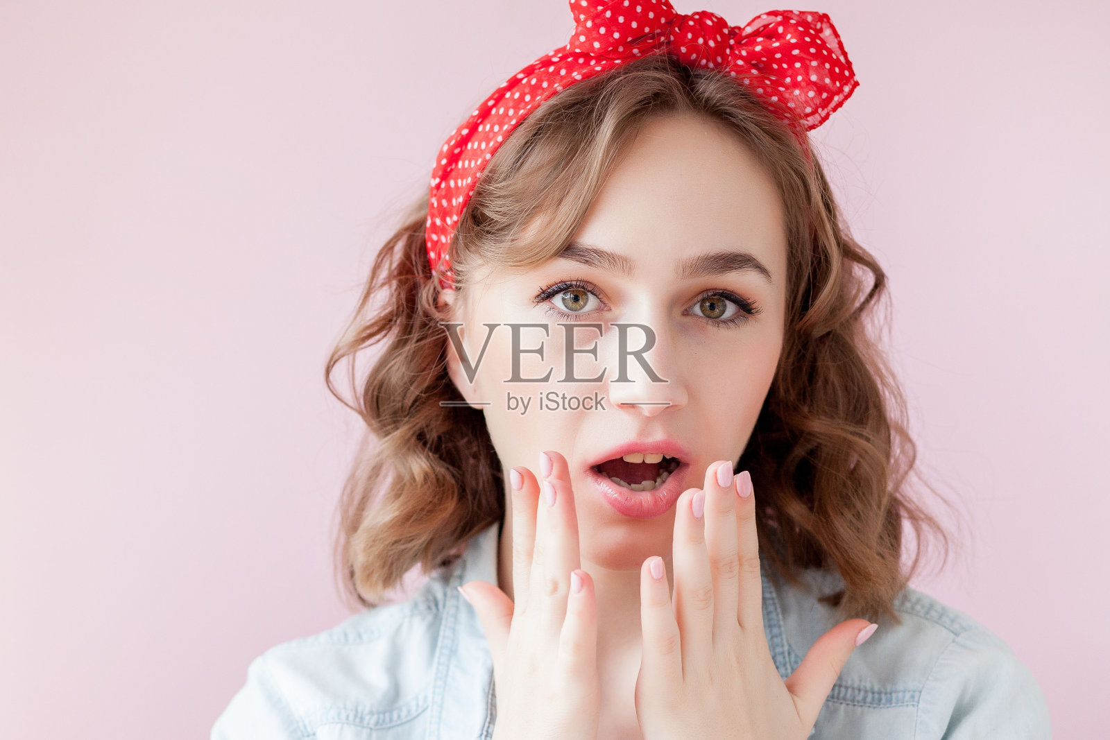 漂亮的年轻女人，有着海报女郎般的妆容和发型。工作室在粉红色的背景上拍摄照片摄影图片