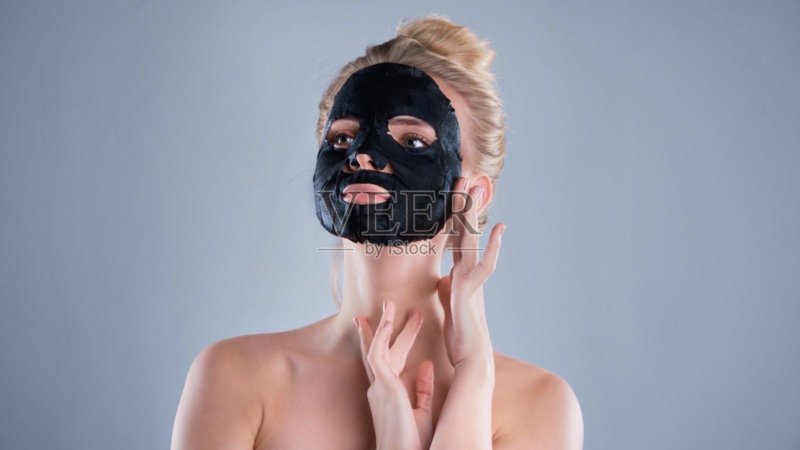 裸肩的女孩在灰色背景下摆姿势，敷着黑色面膜，护肤概念照片摄影图片