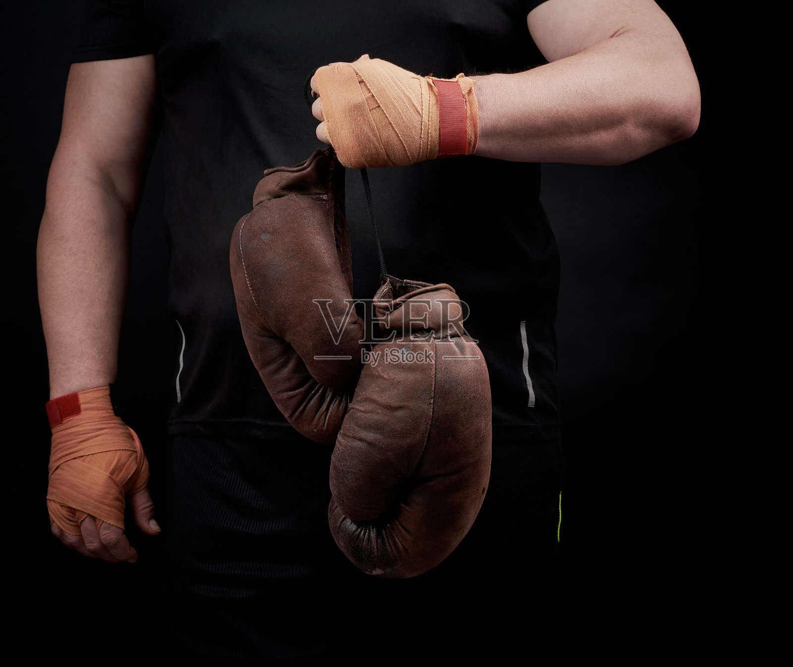 身穿黑色制服的健壮运动员手持棕色旧拳击手套照片摄影图片