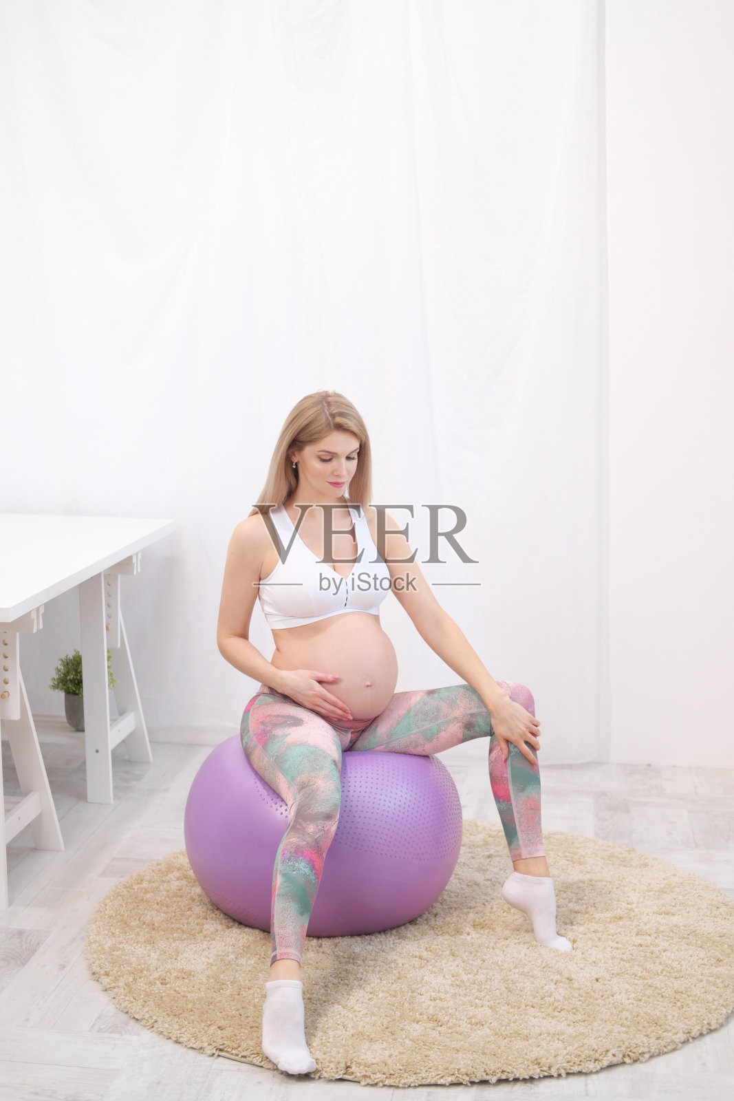 一个年轻漂亮的白人孕妇坐在房子柔软的地毯上。他从事健身运动。运动服装。照片摄影图片