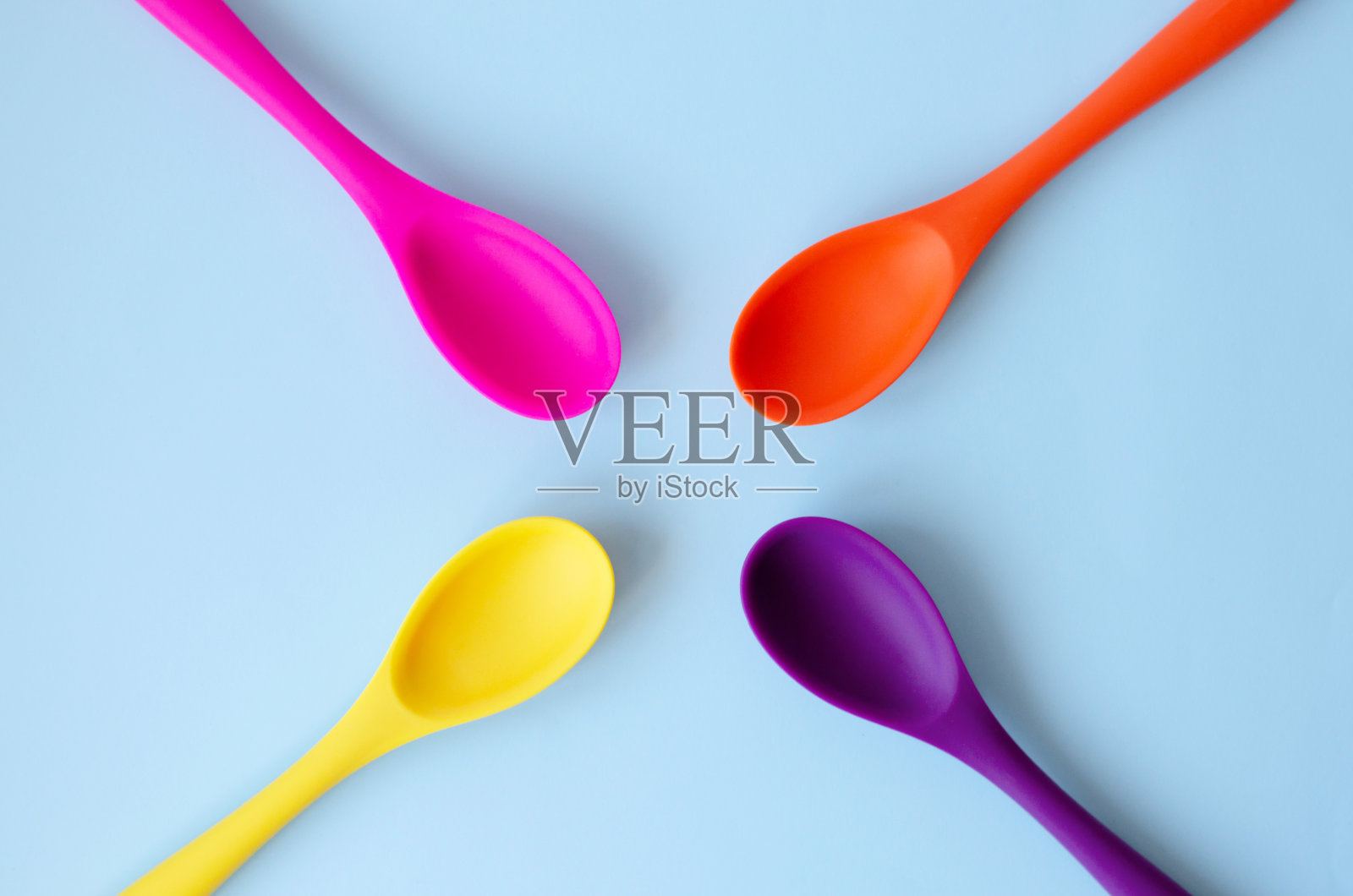 在蓝色背景上平铺一层色彩鲜艳的勺子。照片摄影图片