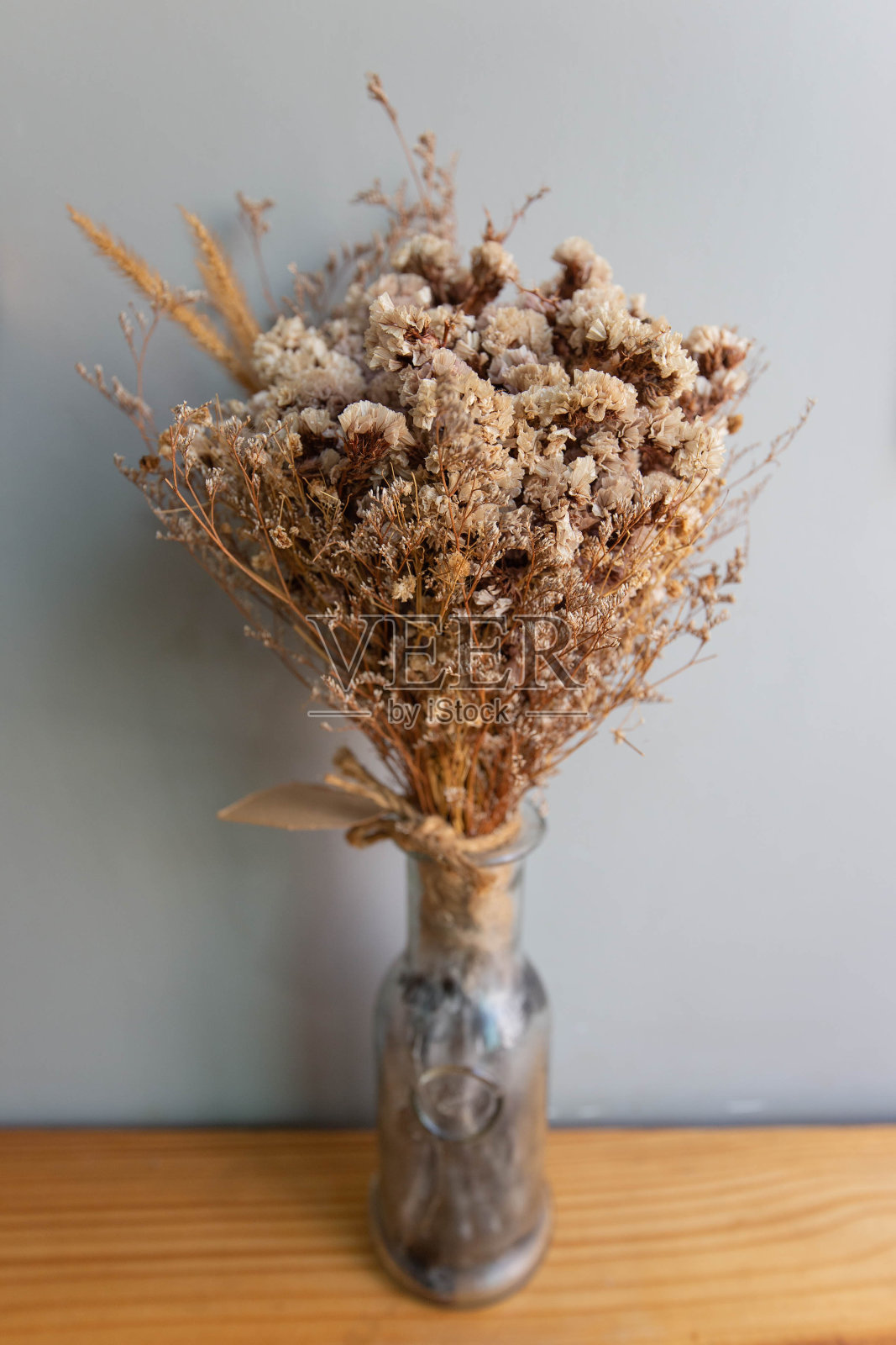 近距离看，一束棕色的干花插在玻璃花瓶里，放在灰色的墙壁后面，木桌上照片摄影图片