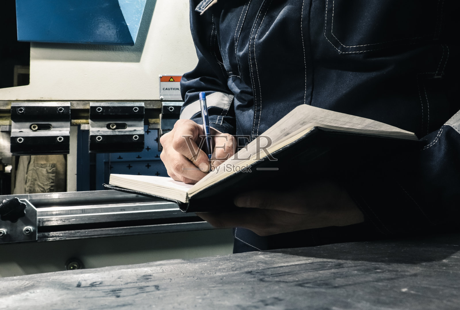 数控机床的操作者在笔记本上记下所做的工作。照片摄影图片