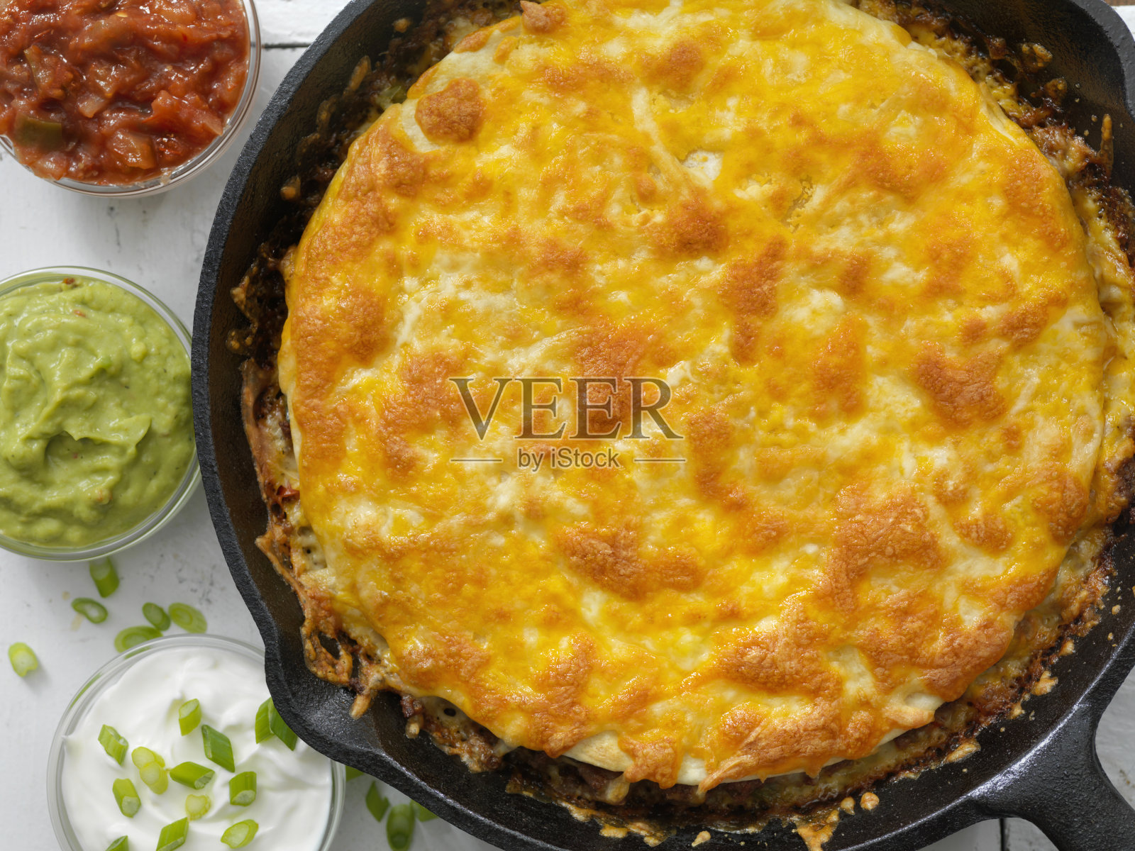 多层牛肉墨西哥饼，在铸铁煎锅中烘烤，配上酸奶油，莎莎酱和鳄梨酱照片摄影图片