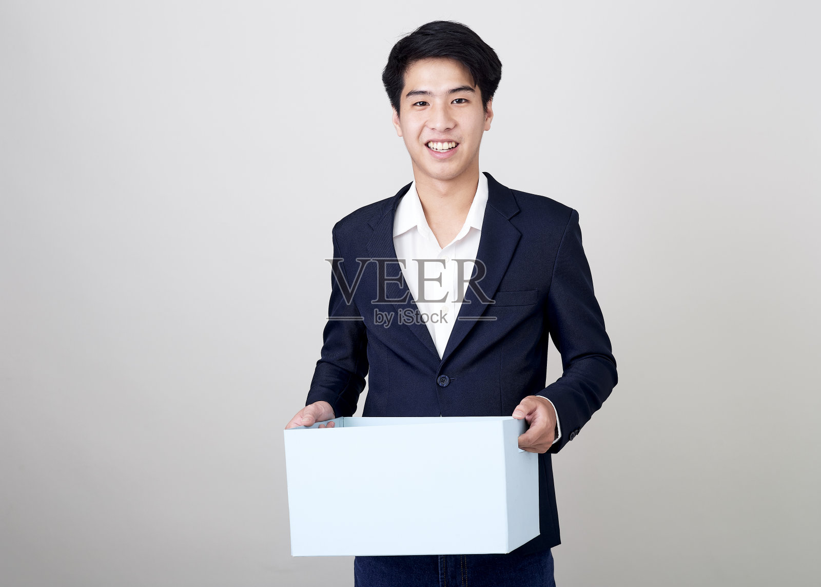 年轻的亚洲商人在工作室里拿着一个盒子，用亮灰色拍摄照片摄影图片
