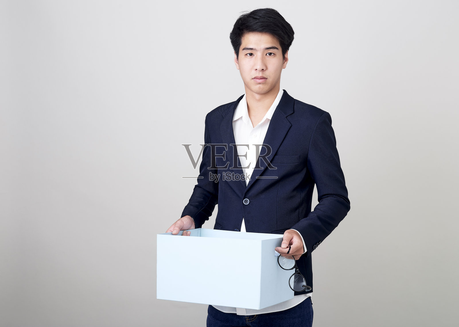 年轻的亚洲商人在工作室里拿着一个盒子，用亮灰色拍摄照片摄影图片