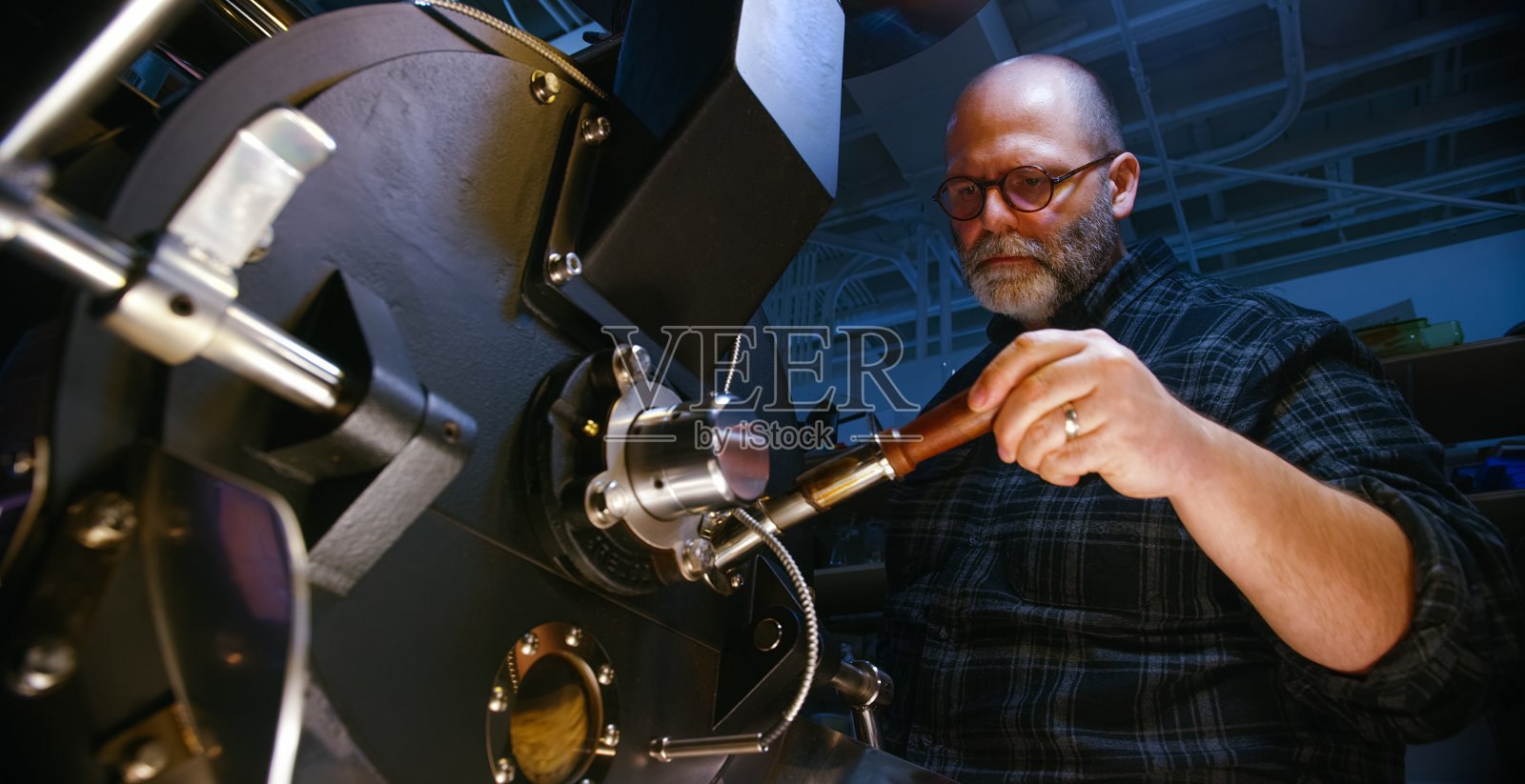 一个四十多岁的白人咖啡烘焙商在室内一个大型商用咖啡烘焙机里检查咖啡豆照片摄影图片