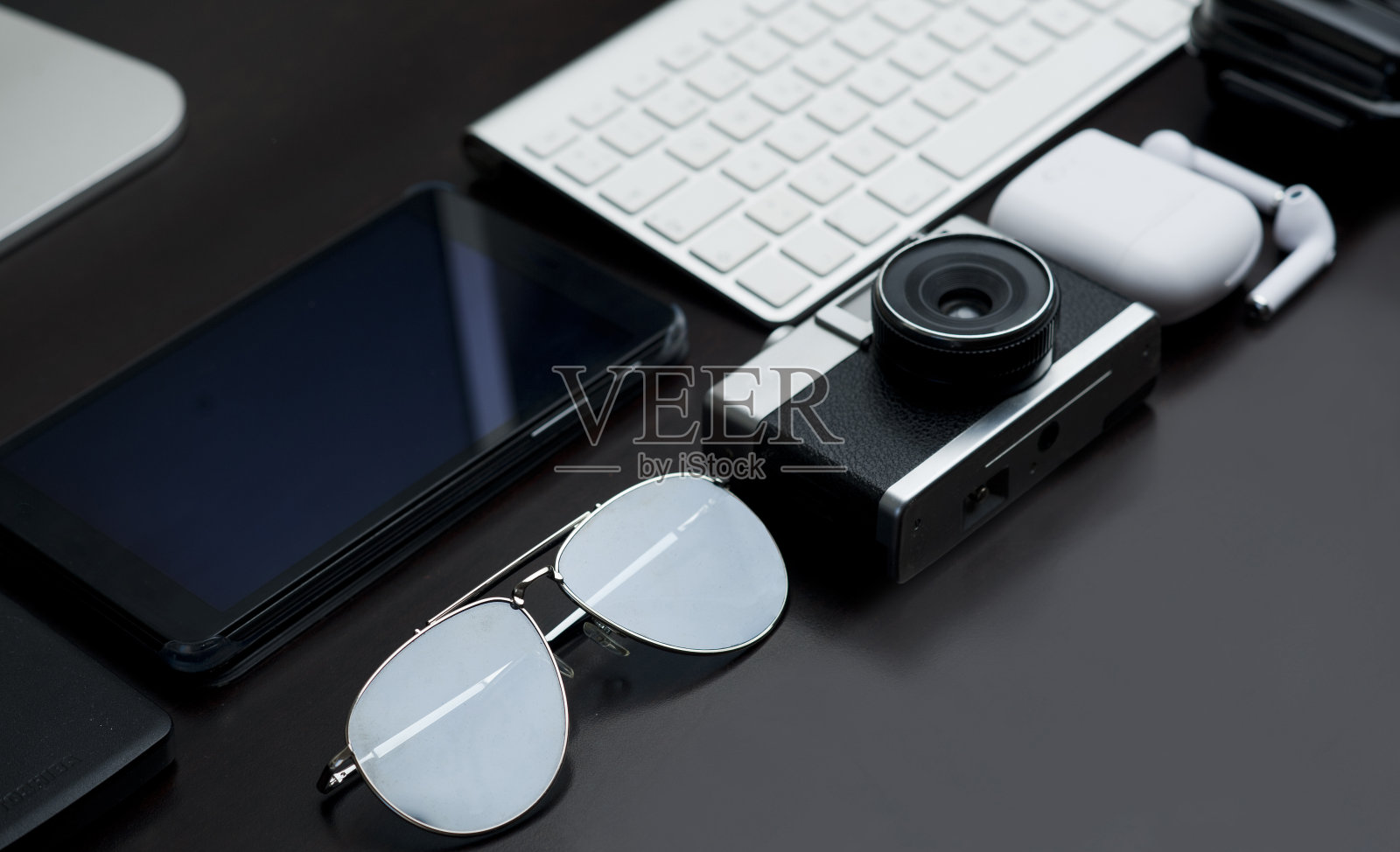 办公桌，配有复古相机，太阳镜，耳机充电器，白色键盘，局部视图防水外壳和银色电脑底座，黑色背景照片摄影图片