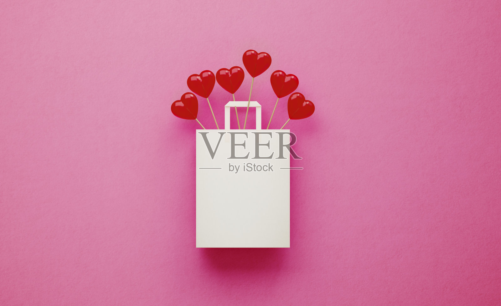 粉色背景下白色购物袋里盛开的心形棒棒糖照片摄影图片