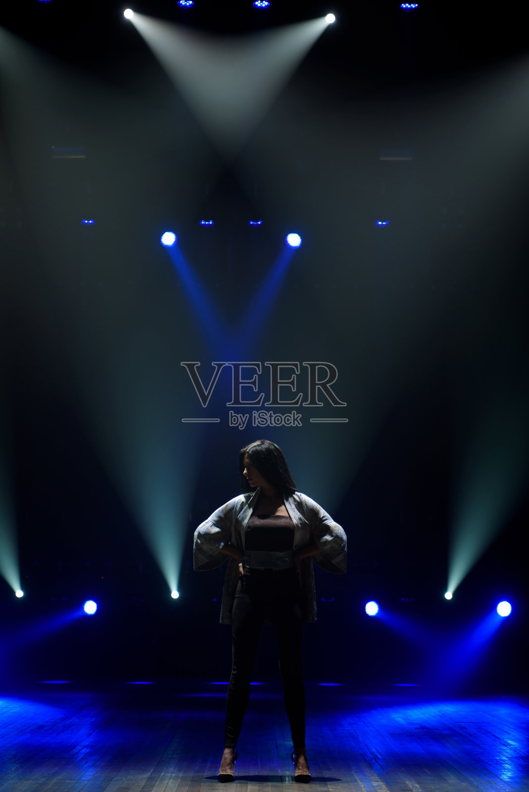 在明亮的蓝色背景下，穿着黑色西装在舞台上表演的女孩照片摄影图片